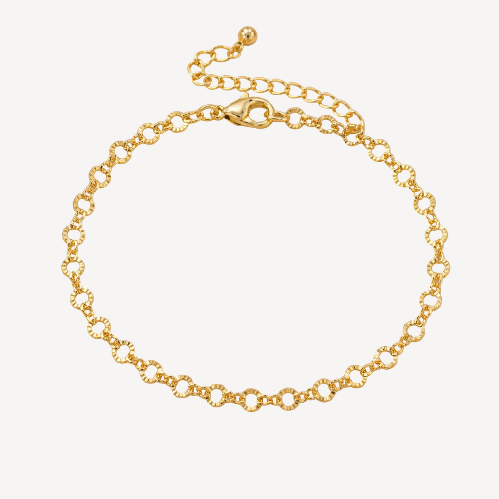 Gold bracelet on a beige surface with dried flowers